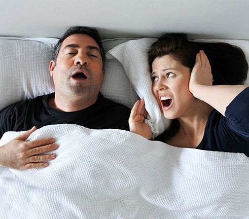 man snoring while wife covers ears