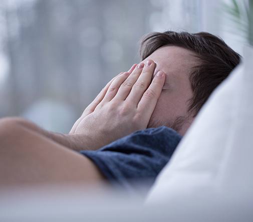 man covering face in bed