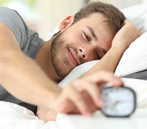 man smiling while turning off alarm clock