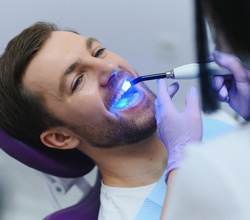 Dentist in blue gloves applying UV light to man’s dental bonding