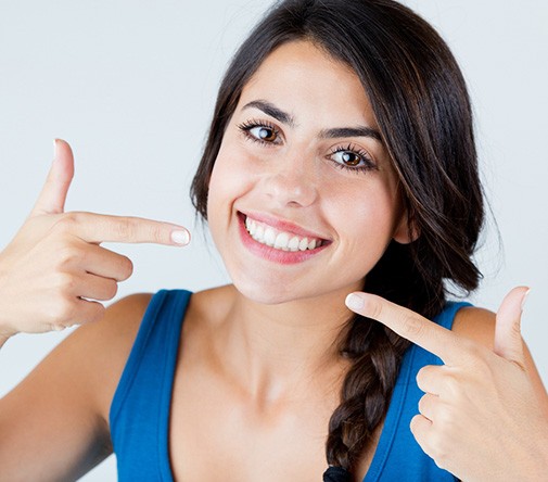 Woman with hair in a braid pointing to her smile