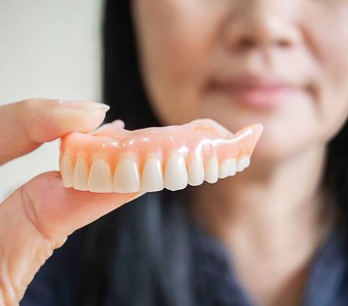 Woman holding upper denture between thumb and forefinger