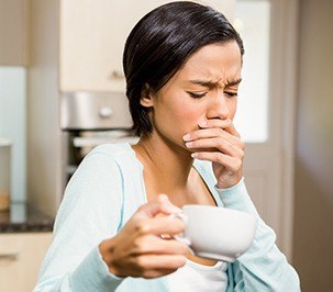 woman holding coffee cup covering mouth with hand