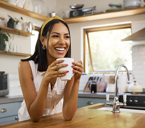 Woman smiling while drinking coffee in kitchen