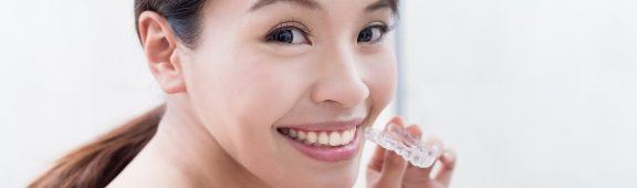 woman holding invisalign tray and smiling at camera