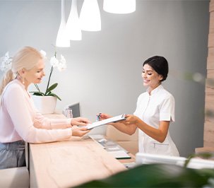 Smiling dental receptionist handing patient form.