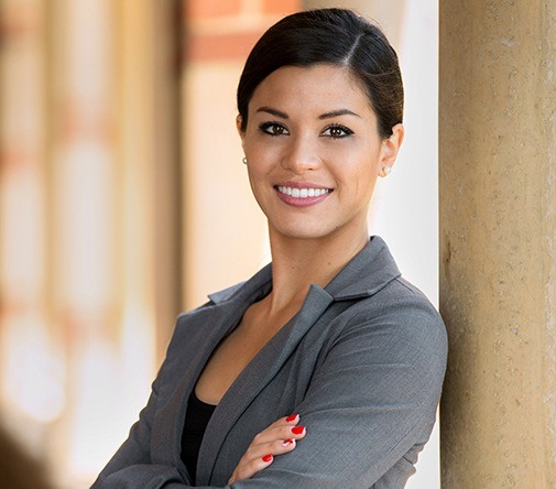 woman in grey suit leaning against pole smiling