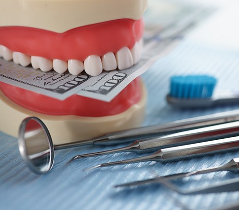 An artificial jaw mockup with money and dental instrument on a table