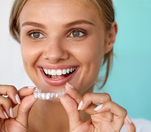A smiling woman applying a teeth whitening tray