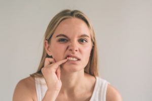Woman with gum disease pokes her gums & should see her dentist