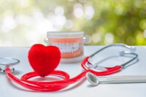 A heart-shaped sponge, a red stethoscope, a dental mold and dental mirror sitting on a gray counter with nature blurred out in the background