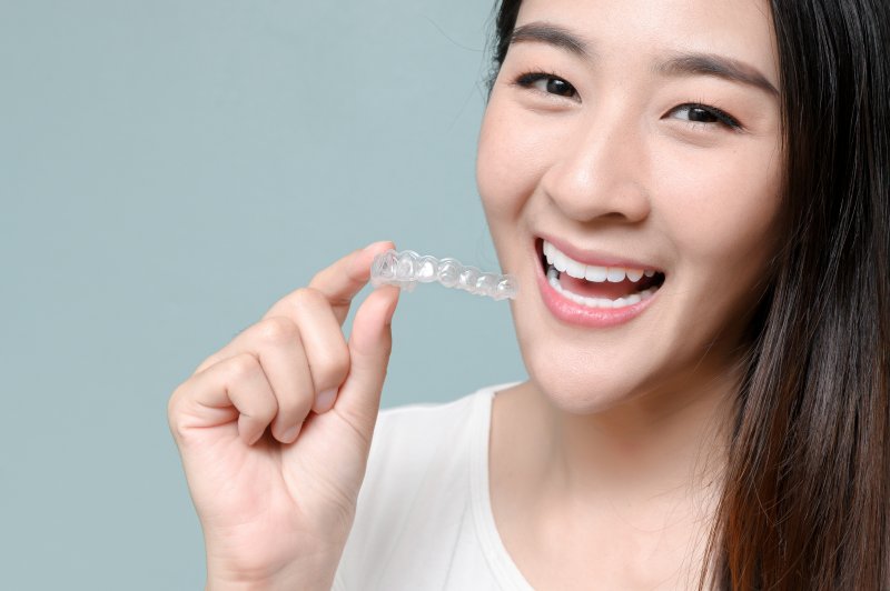 woman smiling and holding Invisalign clear aligner