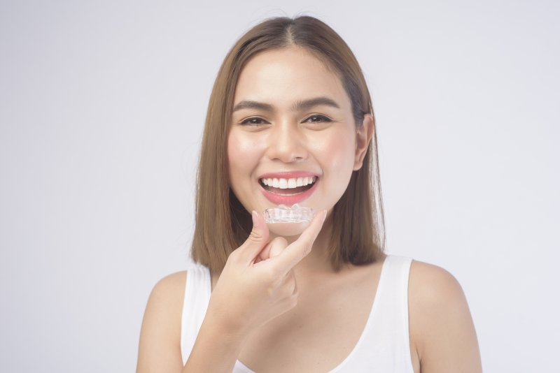 young woman smiling and holding Invisalign aligner