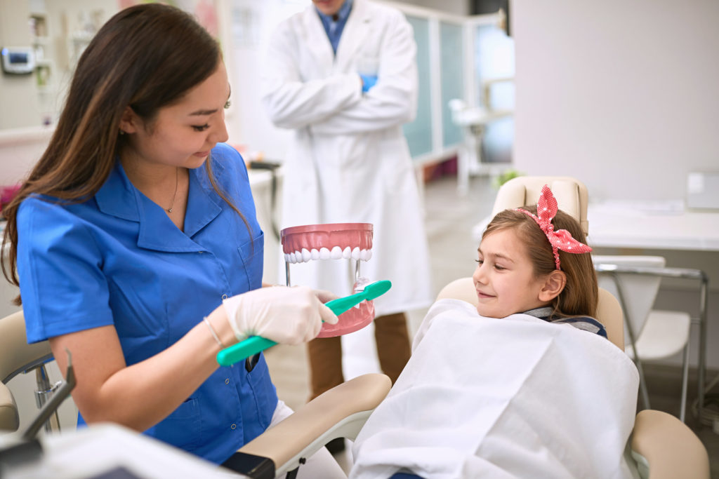 dentist showing child how to brush teeth during cold and flu season in Marysville