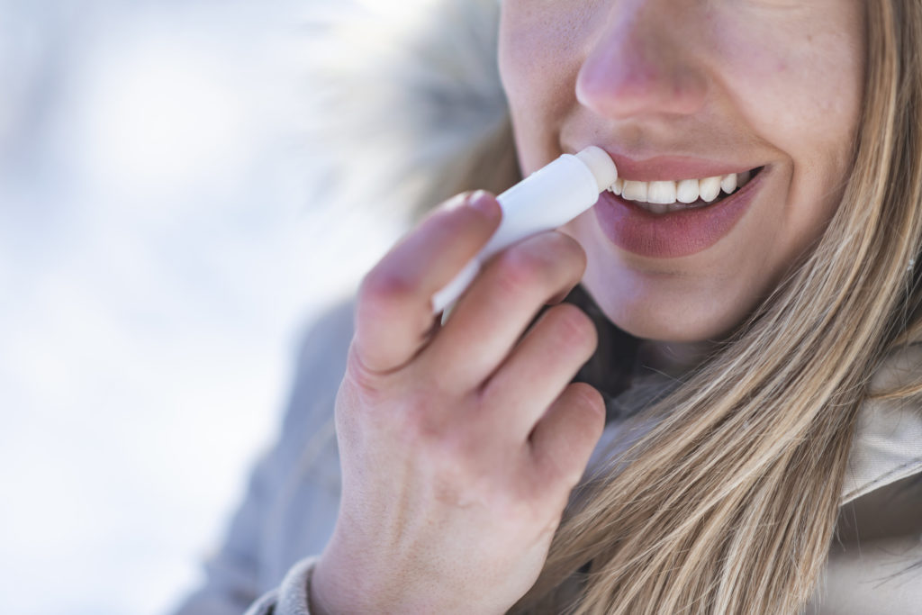 woman applying lip balm to prevent winter mouth issues in Marysville