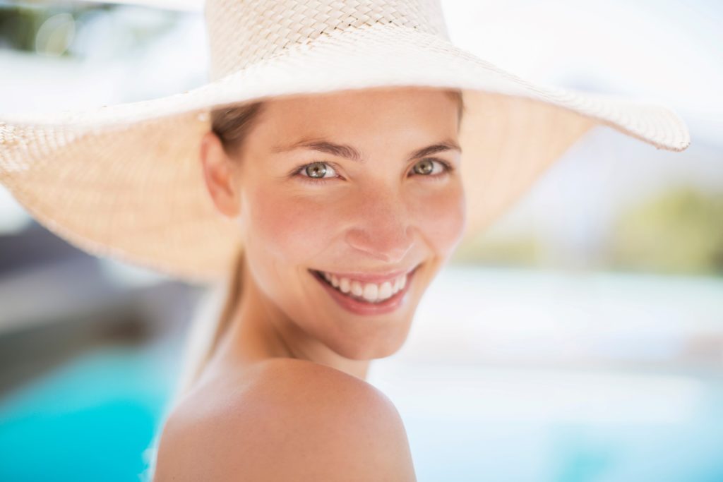 Woman in hat smiling by the pool in summertime