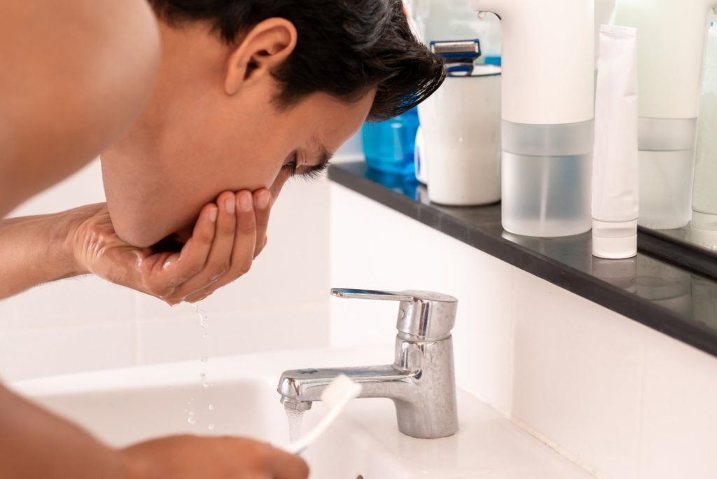 Man rinsing mouth with water after brushing his teeth