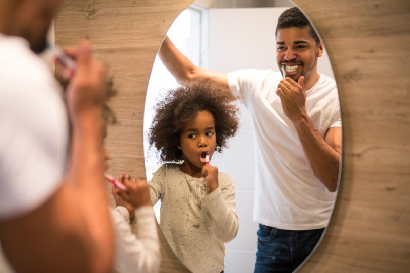 child and their parent brushing in a mirror