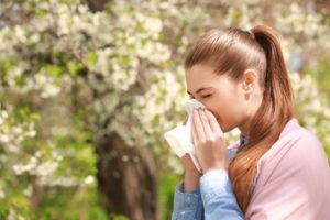 a woman sneezing outside due to seasonal allergies
